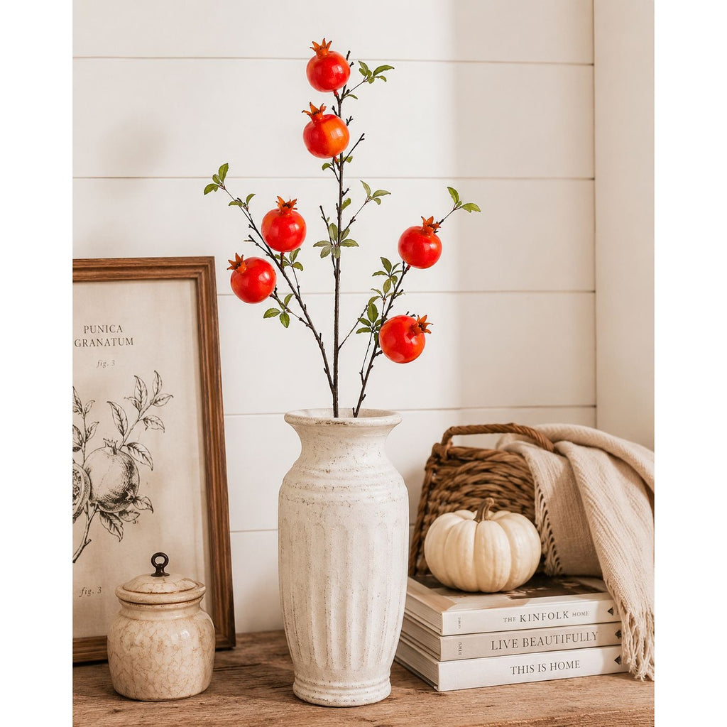 Decorative vase with pomegranate branches on a wooden surface with books and a pumpkin.