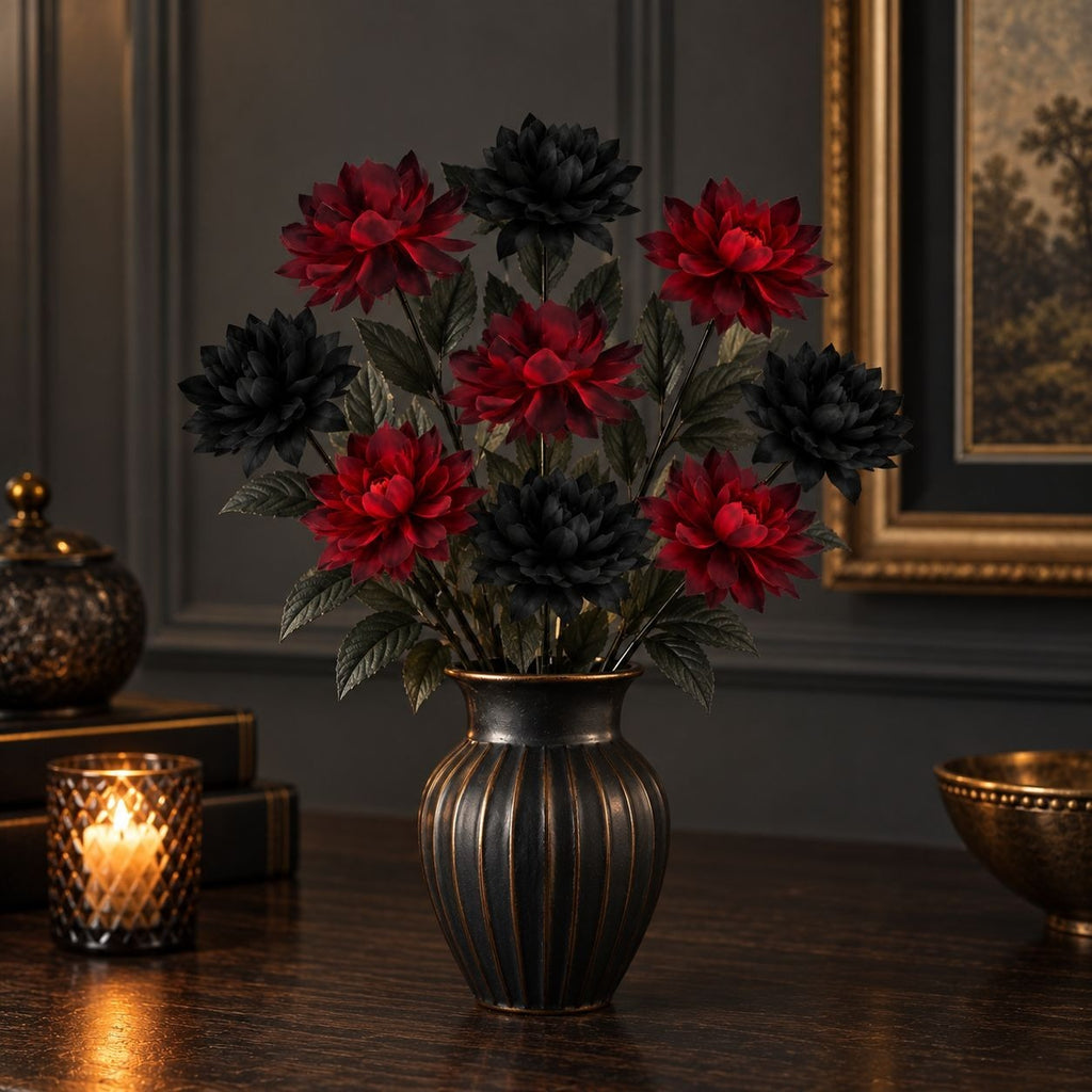 A decorative artificial flower arrangement with alternating deep red and black dahlia-like blooms and green leaves, displayed in a dark ribbed vase on a wooden table in a dimly lit interior setting.