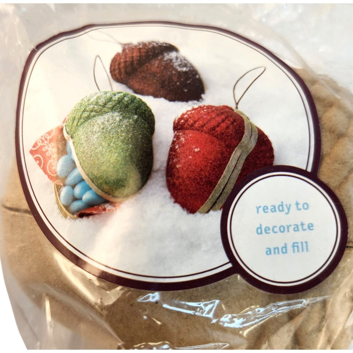 Packaged acorn-shaped craft ornaments in red, green, and brown, shown inside clear plastic wrapping with a printed label that reads 'ready to decorate and fill'.