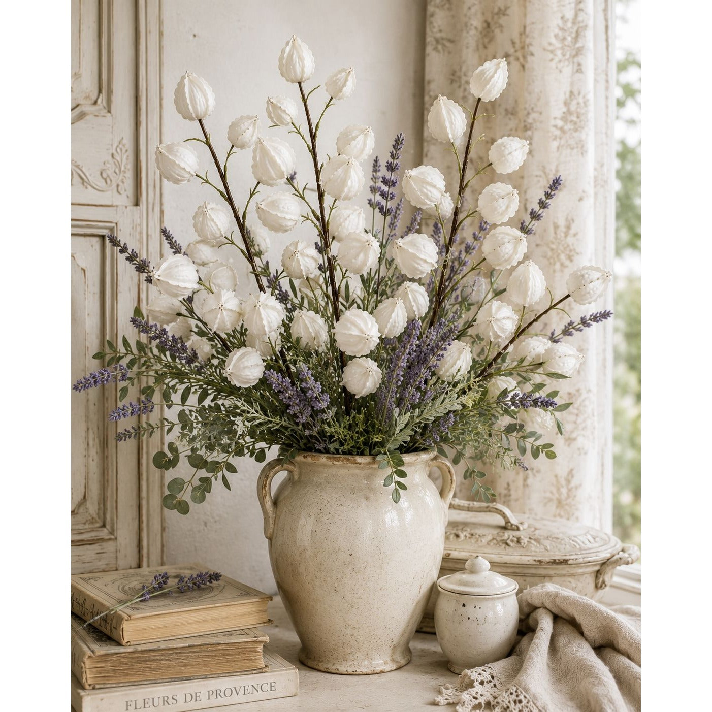 Decorative flower arrangement in a textured vase with books and a blanket in the background.