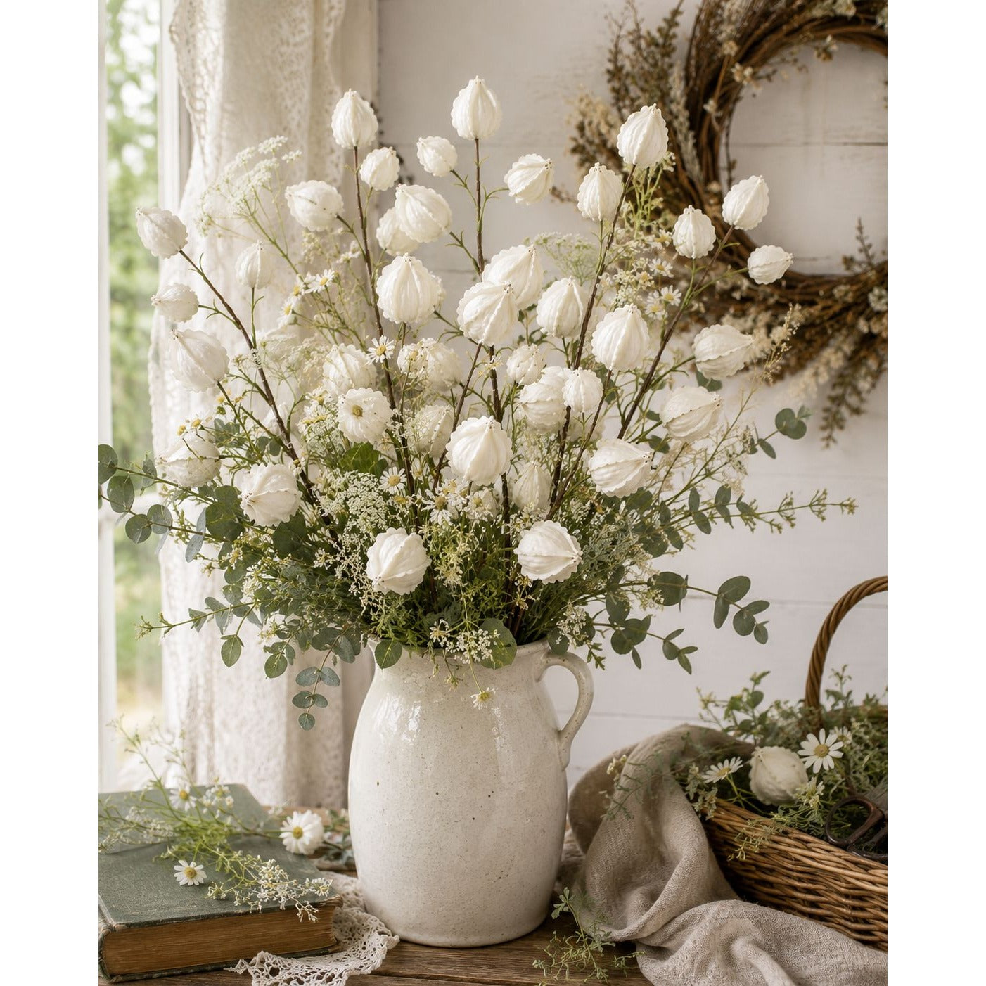 White flowers in a vase on a wooden surface with a decorative wreath in the background.