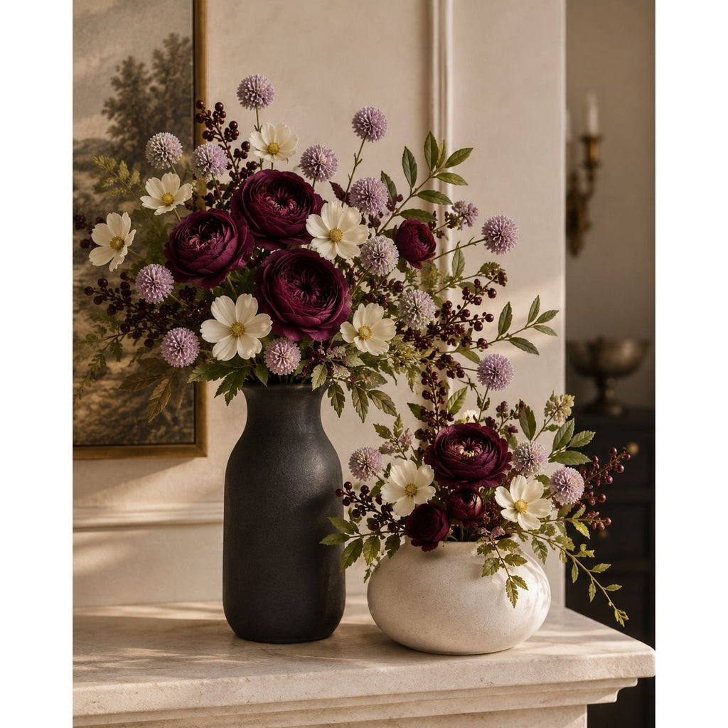 A styled floral arrangement in two vases on a mantel. The larger bouquet is in a matte black vase, and the smaller arrangement is in a cream-colored bowl.