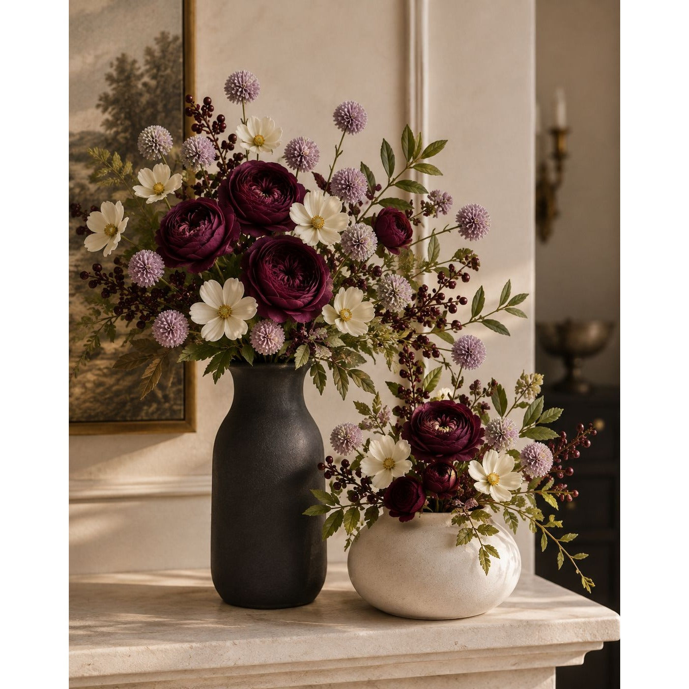 A styled floral arrangement in two vases on a mantel. The larger bouquet is in a matte black vase, and the smaller arrangement is in a cream-colored bowl.