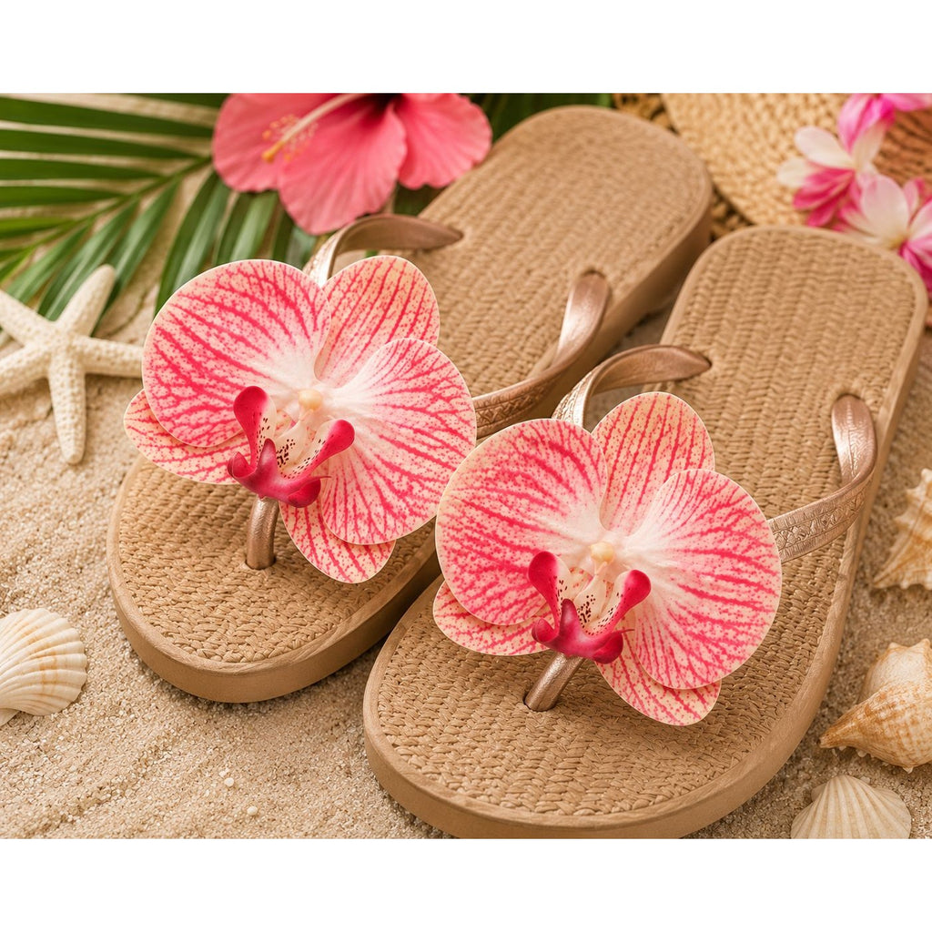 A pair of tan woven flip-flop sandals styled on sand with tropical flowers, starfish, and seashells. Each sandal has a large pink and white orchid flower attached at the thong strap.