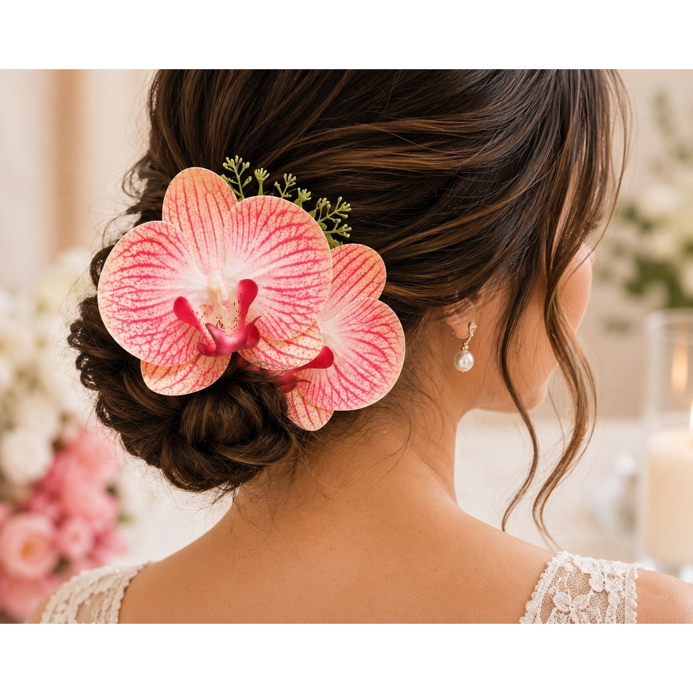 A pink and white orchid flower hair accessory styled in a woman's updo bun, shown from the back. The flower has prominent pink and white striped petals with a bright pink center and small green sprigs, worn next to a pearl drop earring.