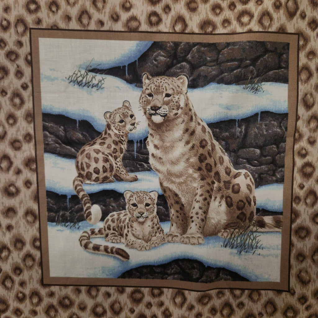 A square textile or wall hanging featuring a painted scene of three snow leopard cubs in a snowy rocky landscape, bordered by a brown patterned fabric.