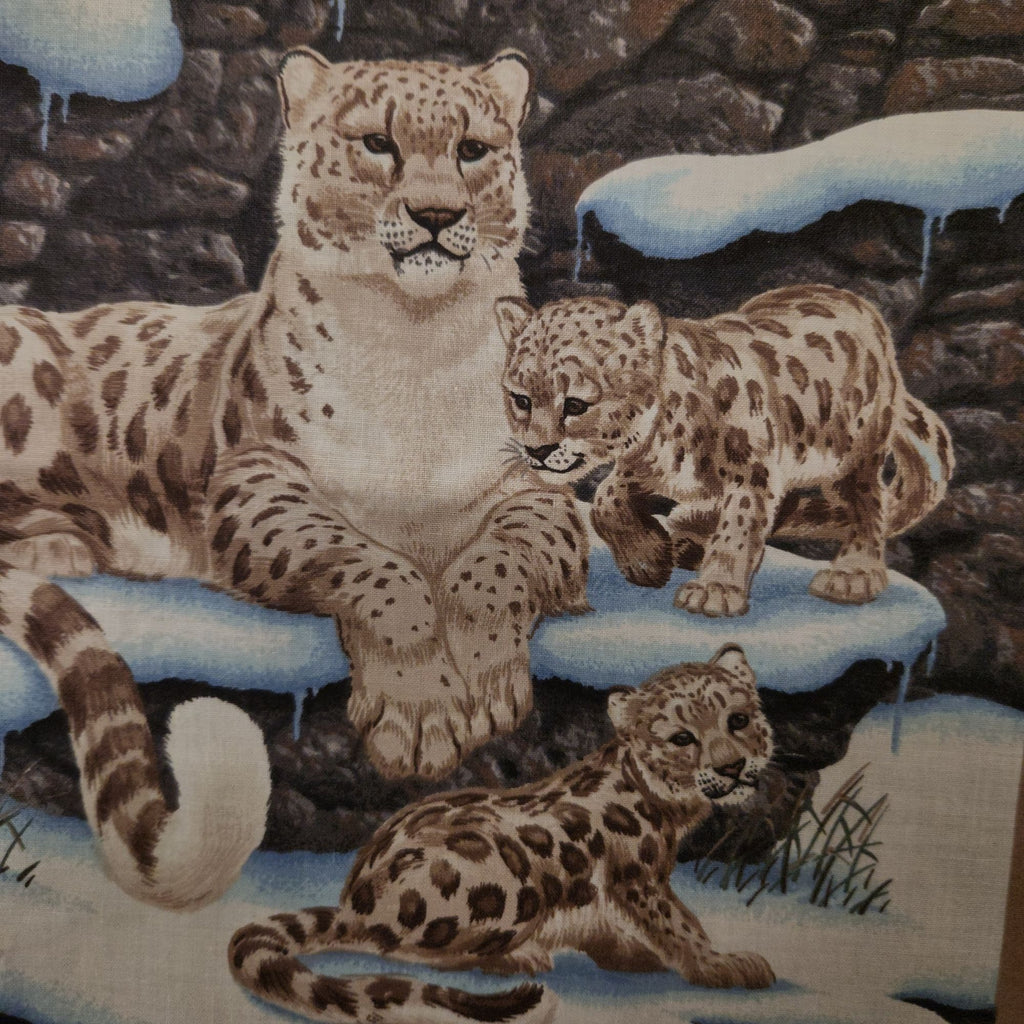 A close-up of a fabric or printed textile featuring three spotted big cat cubs in a snowy rocky setting, with blue snow accents and dark brown rock background.
