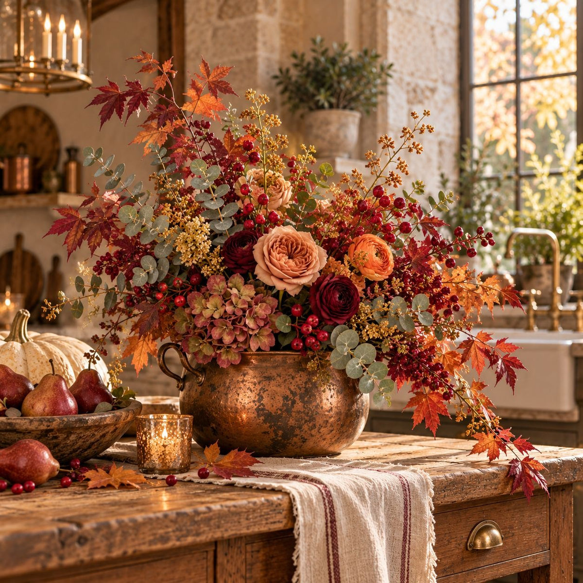A large autumn floral arrangement in a copper-colored metal urn sits on a rustic wooden kitchen counter. The arrangement features fall leaves, red berries, hydrangeas, and peach roses, with a warm, cozy kitchen background visible through the window.