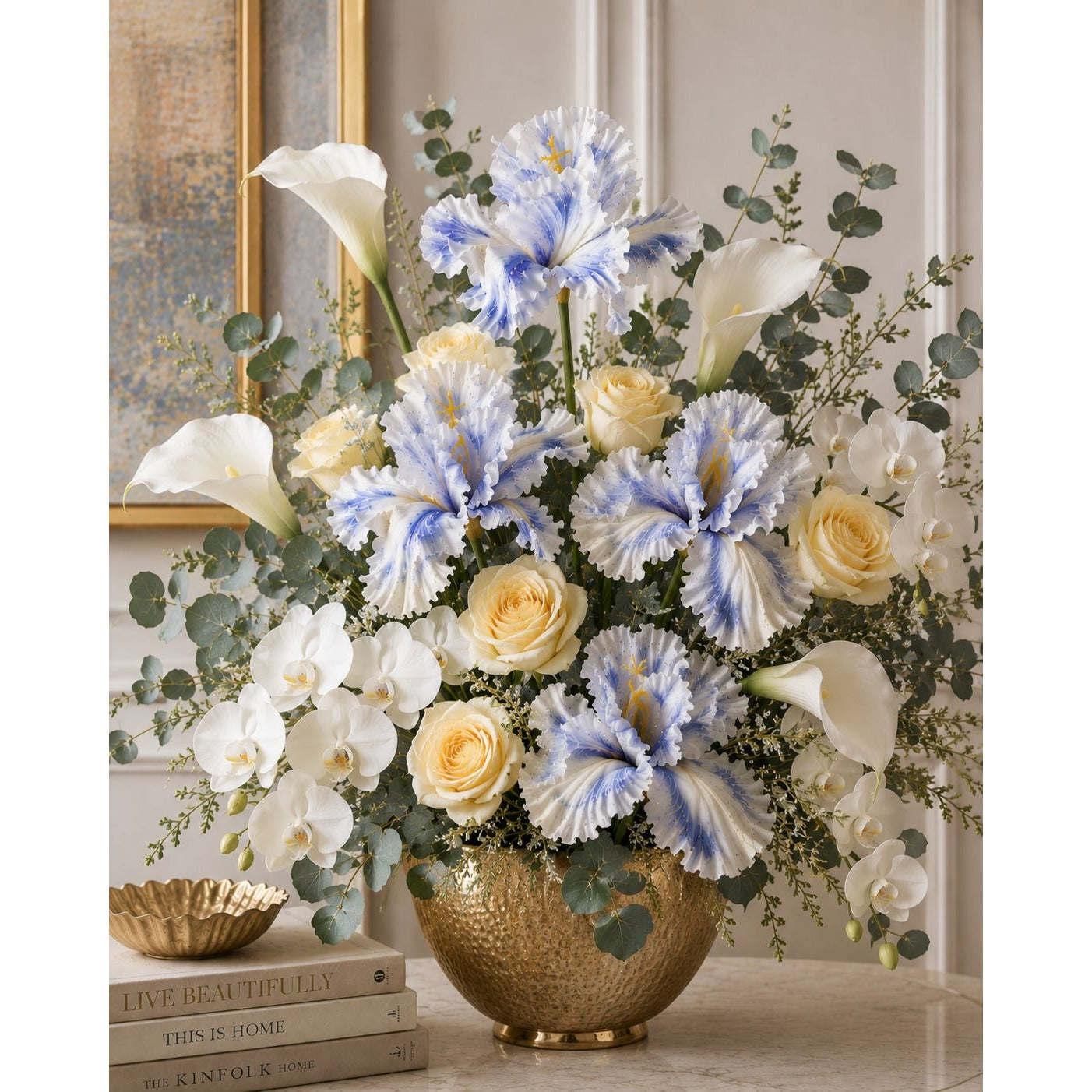 Floral arrangement with blue, white, and yellow flowers in a gold vase on a table.