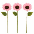 Three artificial pink sunflowers with green stems and leaves, arranged vertically on a plain white background.