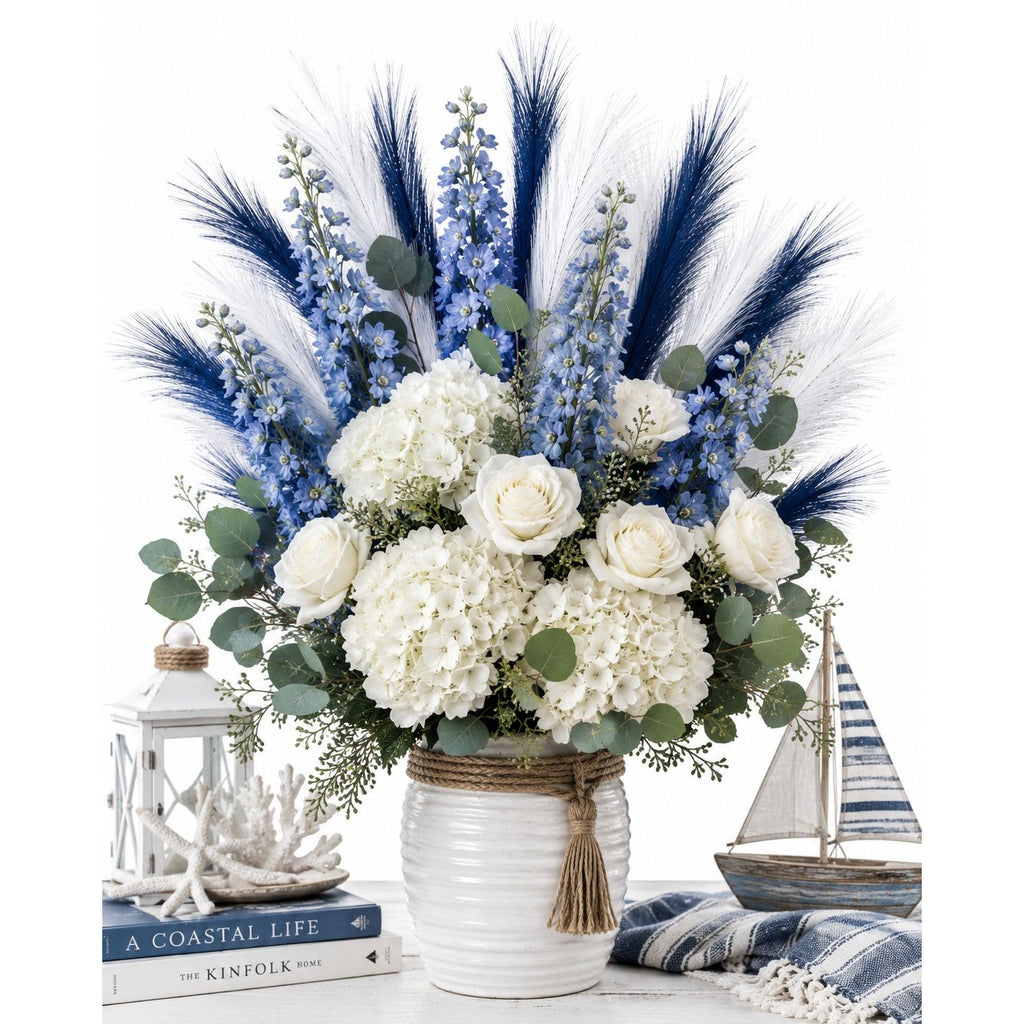Floral arrangement with white flowers, blue accents, and eucalyptus in a white vase, with a coastal theme.
