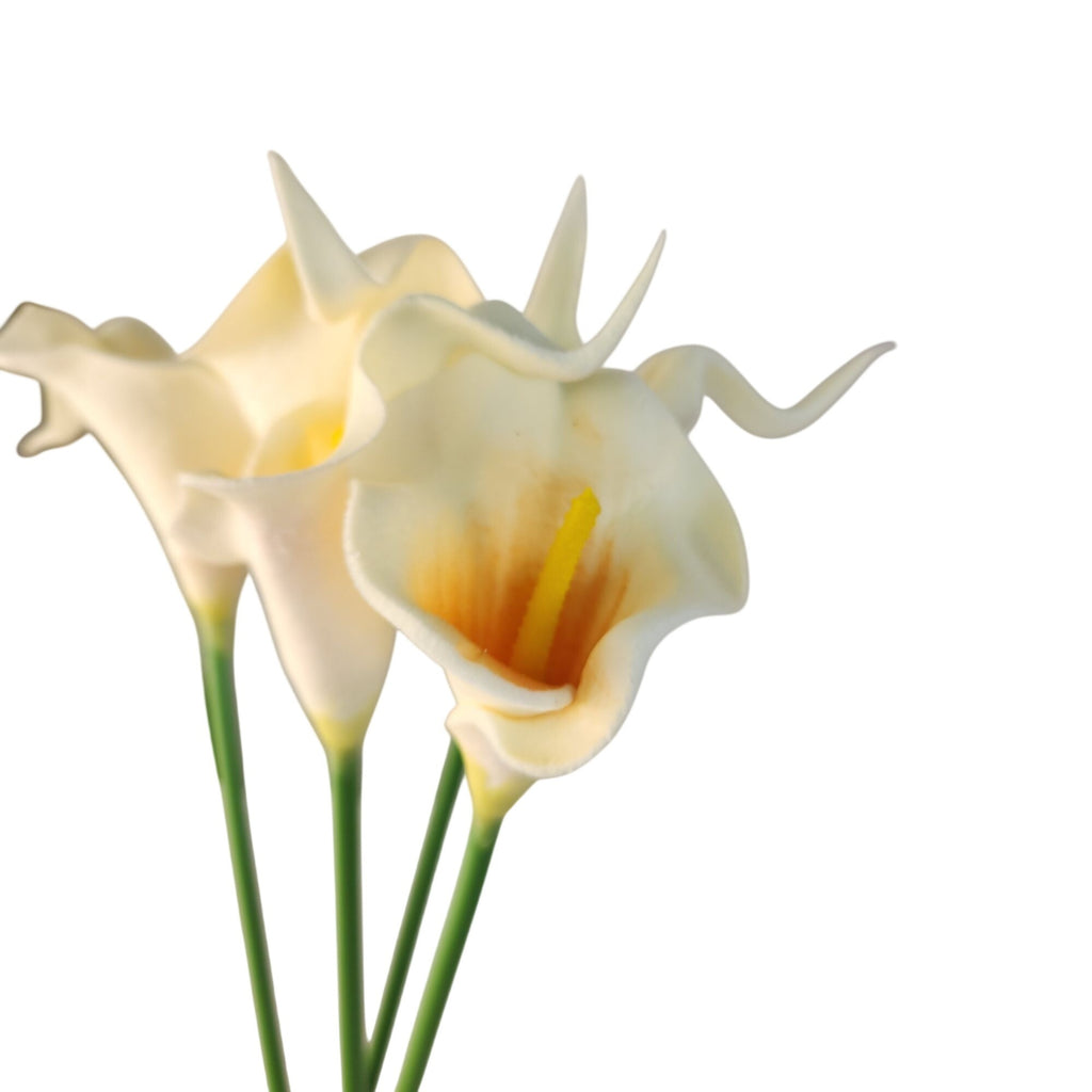 Three artificial calla lilies with cream-colored blooms, yellow centers, and green stems on a plain white background.