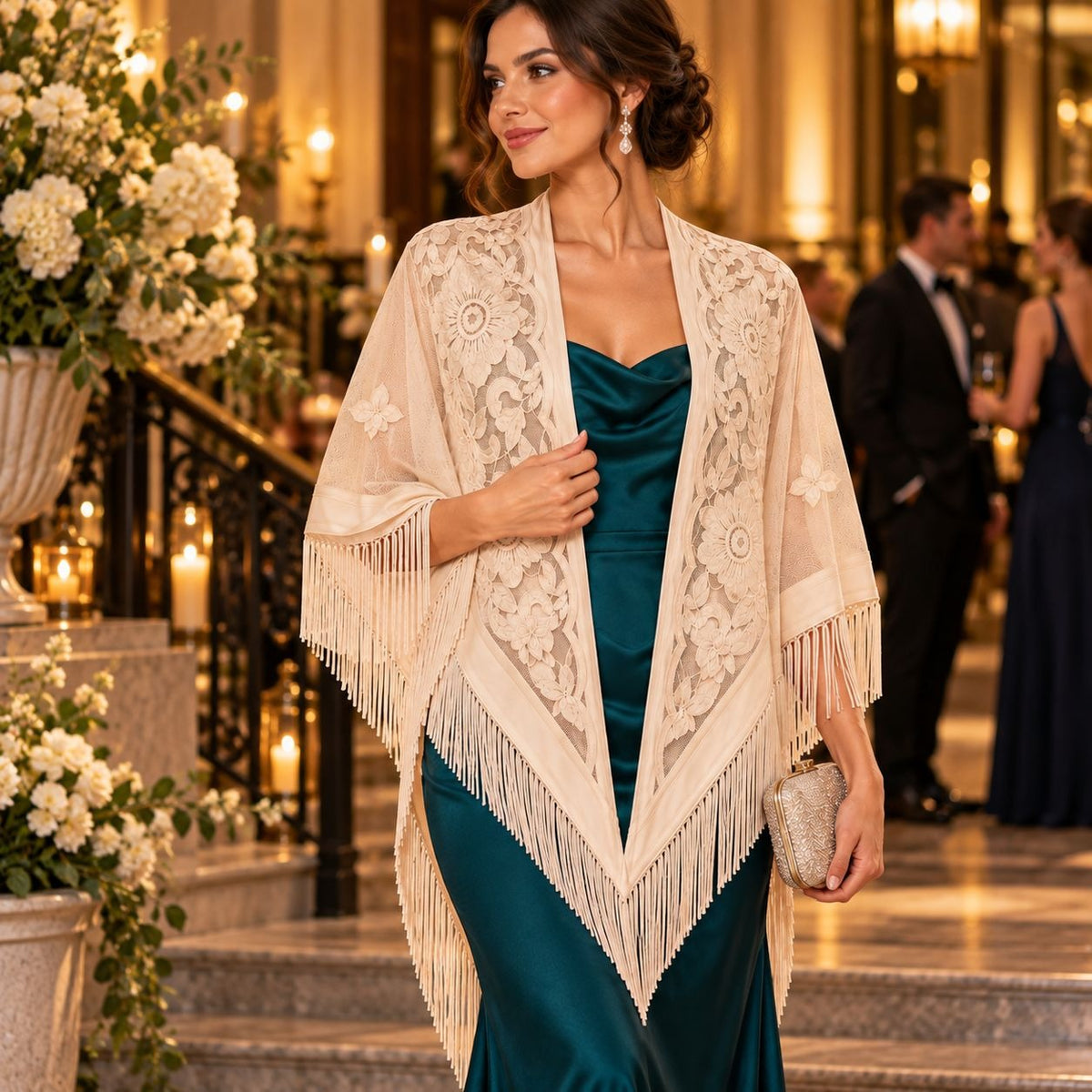 A woman in a formal event setting wearing a cream lace and fringe shawl over a teal satin gown, holding a small metallic clutch.