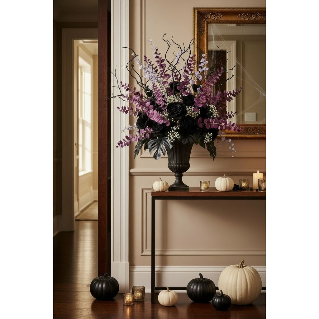 A large artificial floral arrangement in a black urn vase sits on a console table in a decorated indoor hallway. The bouquet features black roses, purple wisteria-like stems, and white filler flowers with dark branches.