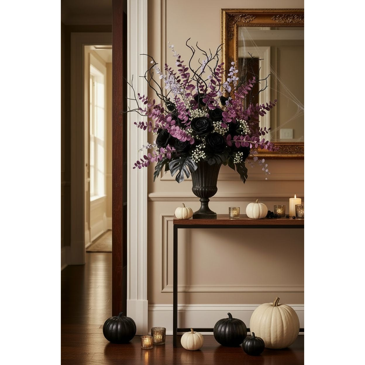 A large artificial floral arrangement in a black urn vase sits on a console table in a decorated indoor hallway. The bouquet features black roses, purple wisteria-like stems, and white filler flowers with dark branches.