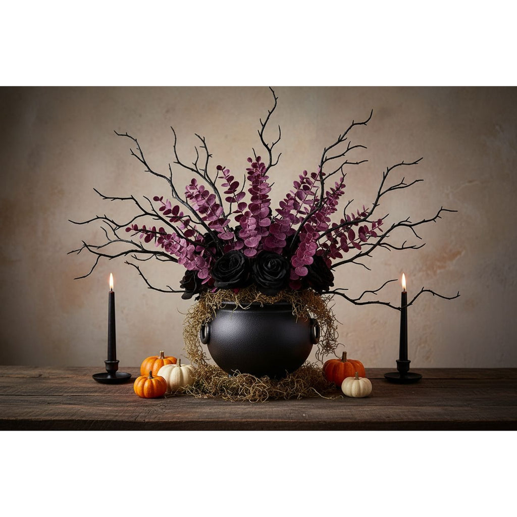 A gothic-style floral arrangement in a black cauldron vase with purple flowers, black roses, and bare branches, displayed on a rustic wooden table with lit black candles and small pumpkins against a textured beige backdrop.