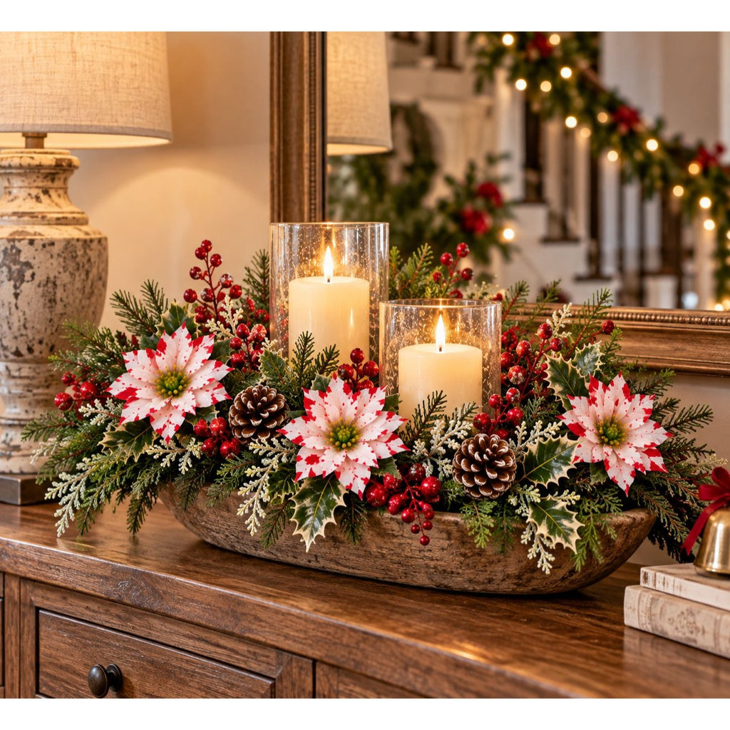 A rustic wooden bowl holiday centerpiece filled with green pine branches, white berries, pinecones, and three lit white pillar candles in clear glass holders, displayed on a wooden console table in a warmly lit room.