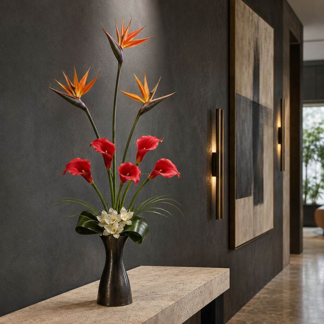 A floral arrangement in a dark vase on a stone console table, featuring orange bird of paradise flowers, red calla lilies, and small white blossoms, set in a modern hallway with a dark textured wall and wall art.