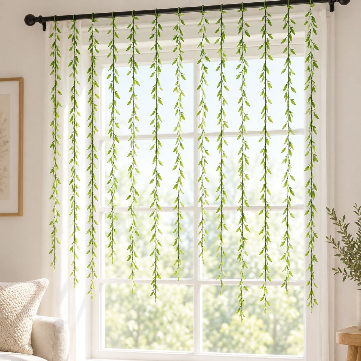Green hanging leaf curtain panels on a black rod in front of a bright window, shown in a styled room setting with a sofa and framed art partially visible.