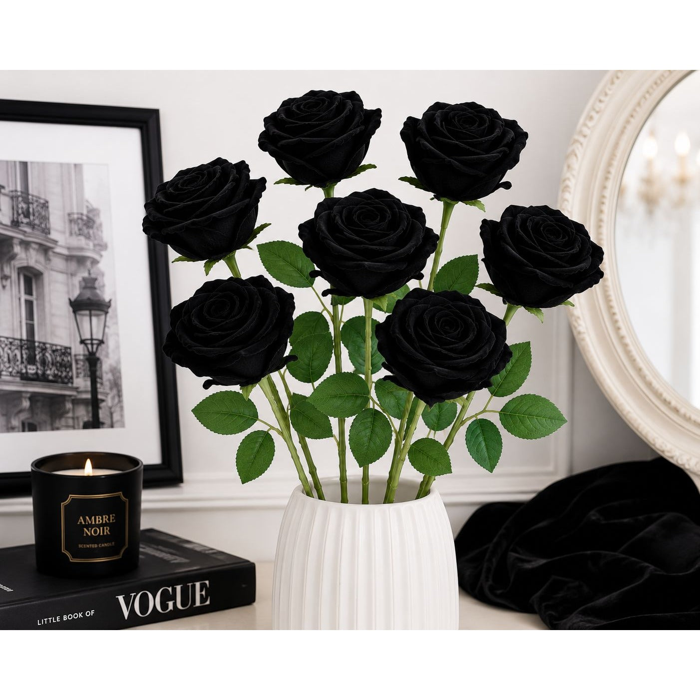 Bouquet of black roses in a white vase on a table with a candle and magazine in the background.