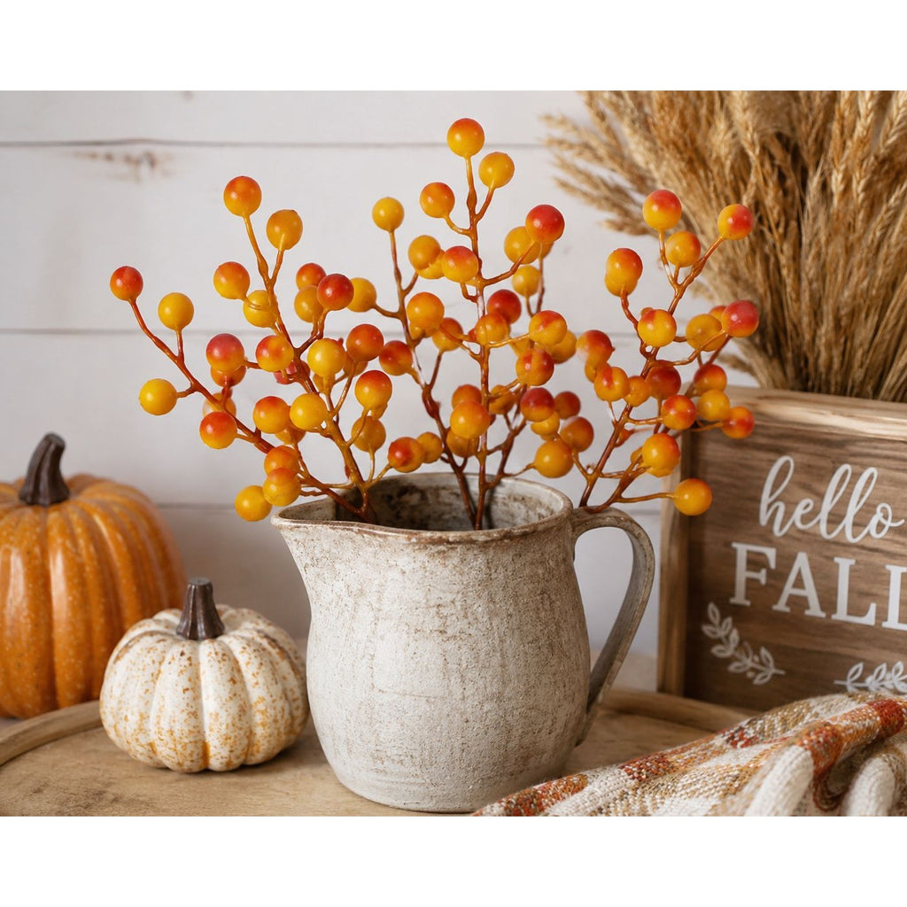 Decorative setup with a pitcher of berries, pumpkins, and a 'hello FALL' sign on a wooden surface.