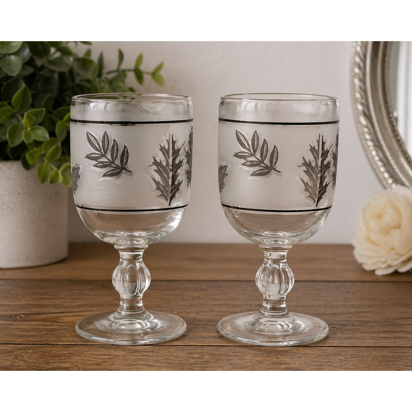 Two decorative glass goblets with leaf patterns on a wooden surface.