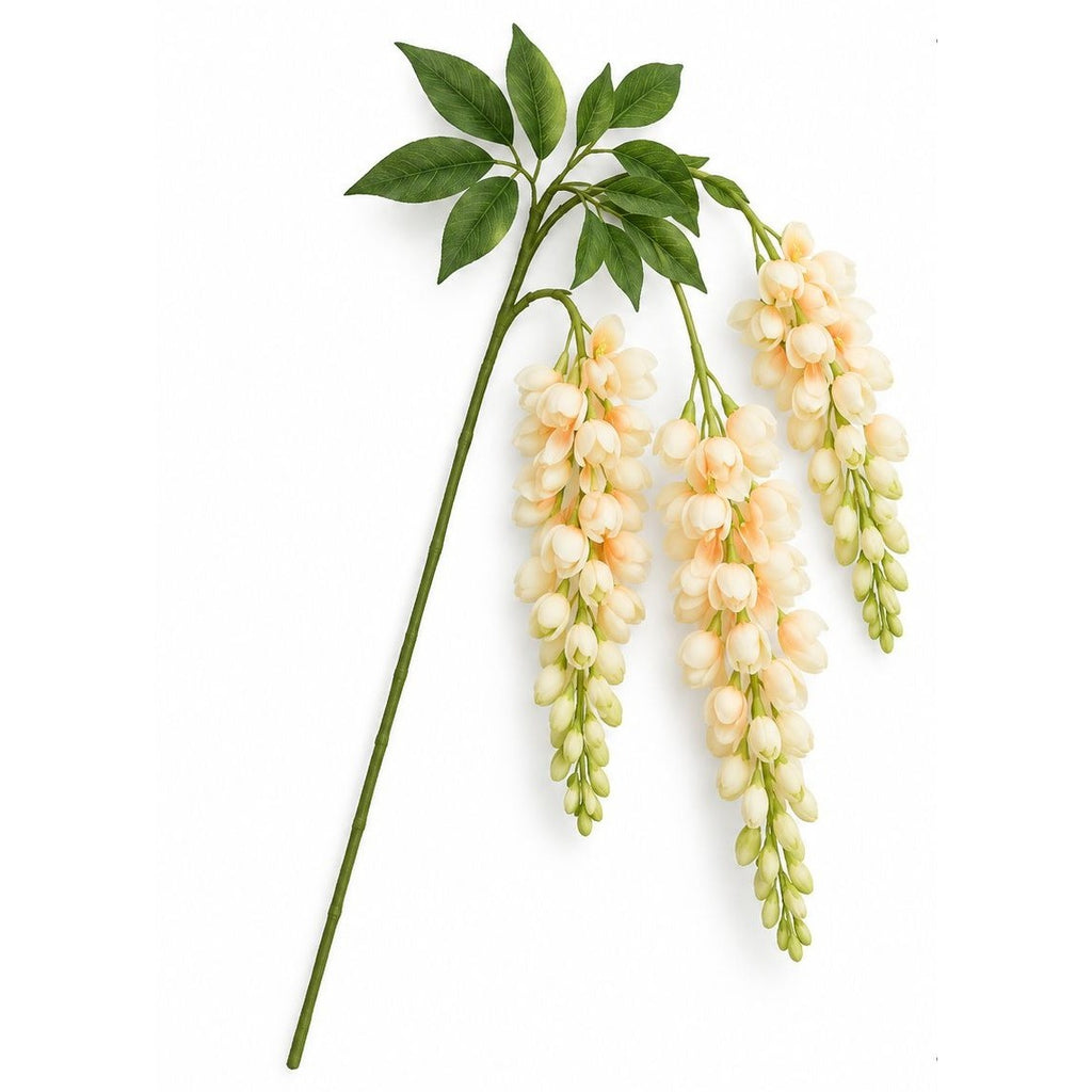 An artificial wisteria flower stem with pale peach and cream blossoms, green leaves, and a long green stem, photographed on a plain white background.