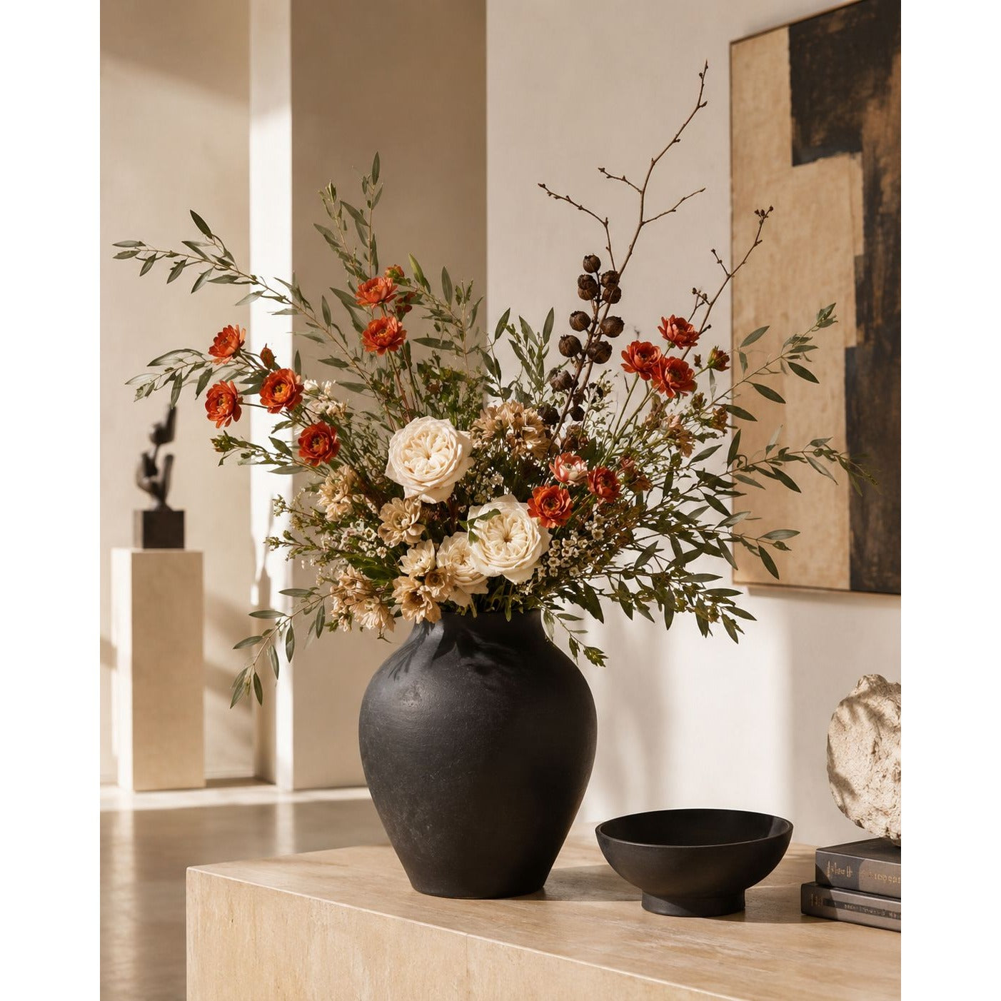 A dark matte ceramic vase filled with a dried floral arrangement featuring red-orange berries, cream roses, and green foliage, displayed on a light wood console table in a modern interior setting.
