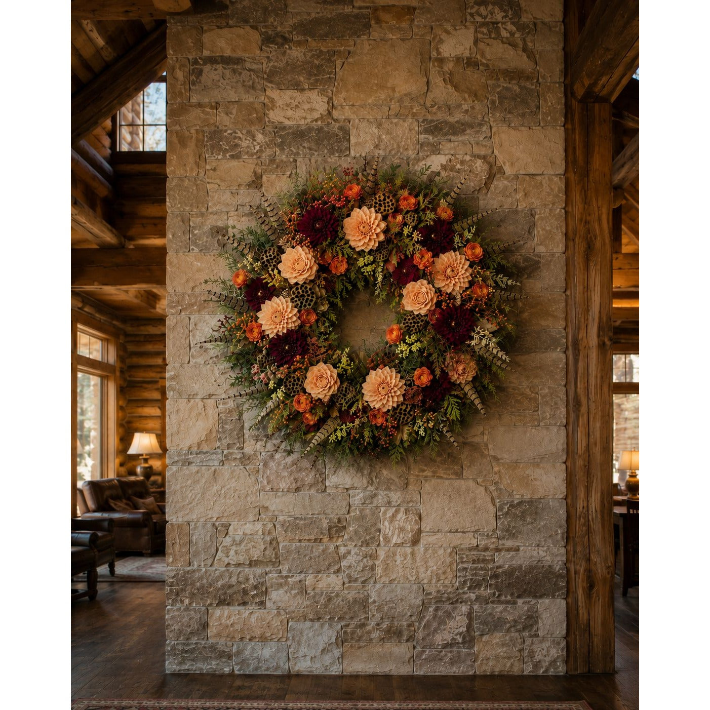 An autumn floral wreath with orange, burgundy, and cream flowers, hung on a rustic stone pillar inside a cozy lodge-style room with wooden beams and a fireplace.