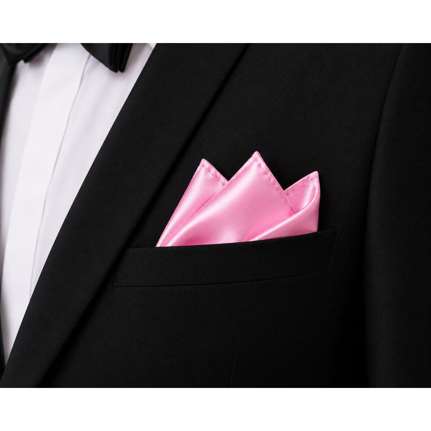 A close-up of a black tuxedo jacket with a white dress shirt and black bow tie, featuring a bright pink satin pocket square folded neatly in the breast pocket.