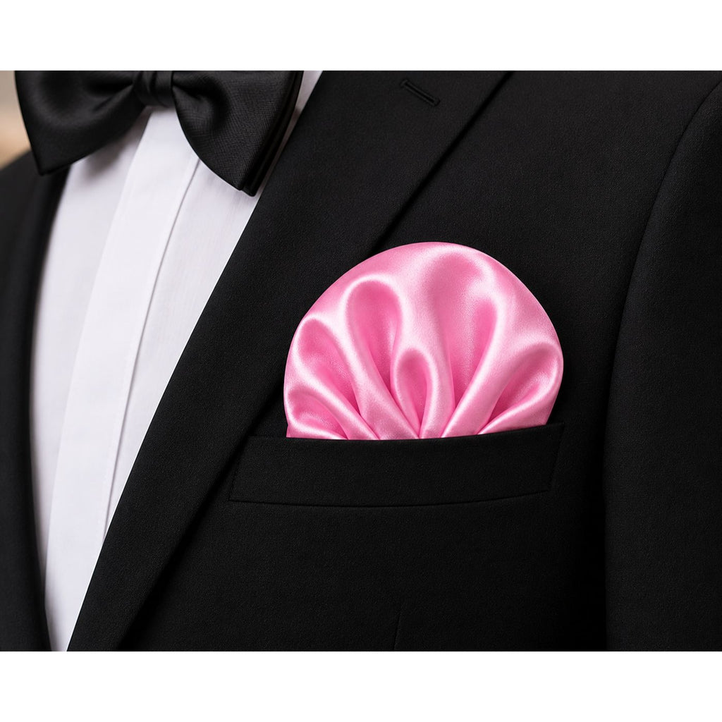 A close-up of a black tuxedo jacket with a white dress shirt, black bow tie, and a bright pink satin pocket square in the breast pocket.