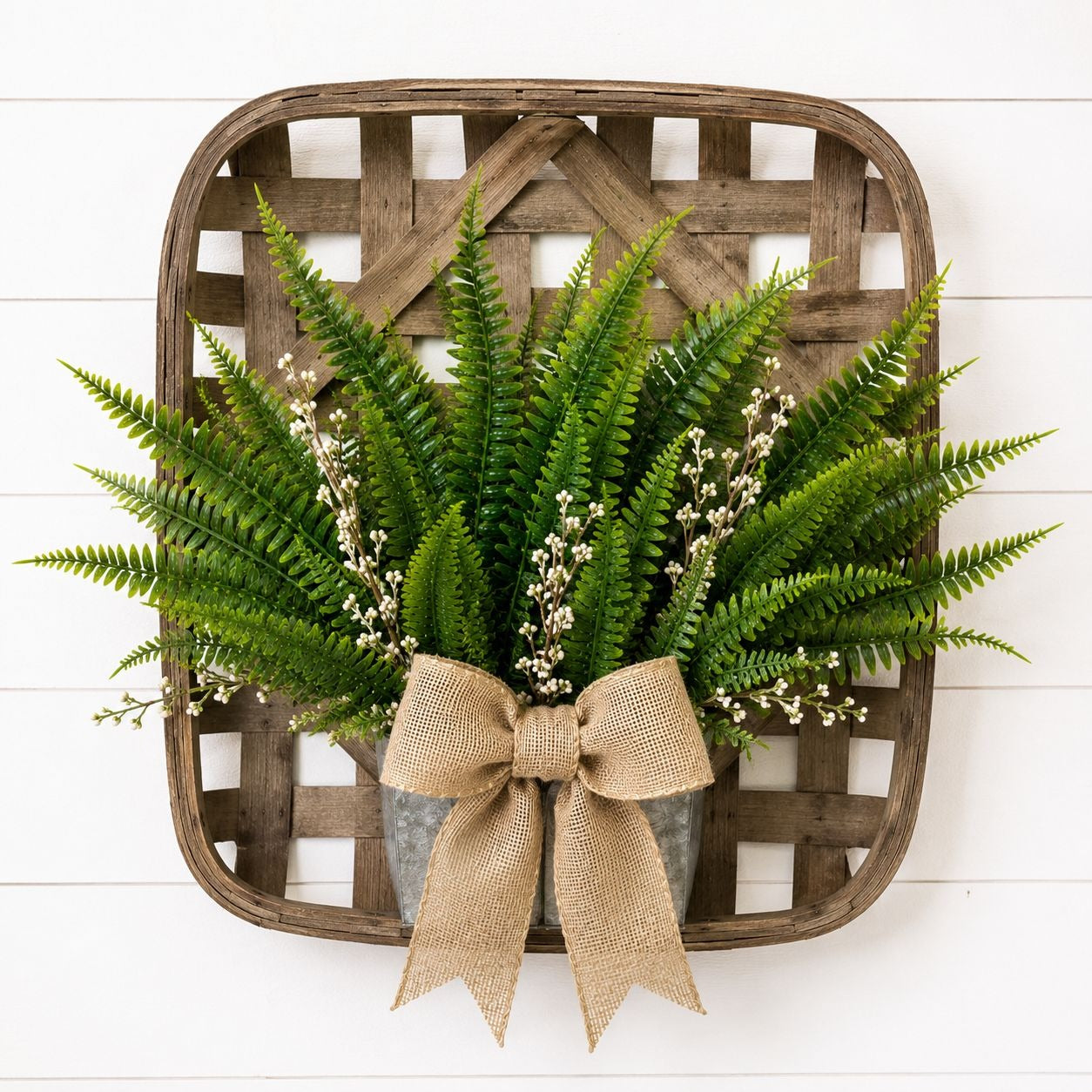 Fern wreath with a burlap bow on a wooden basket against a white background