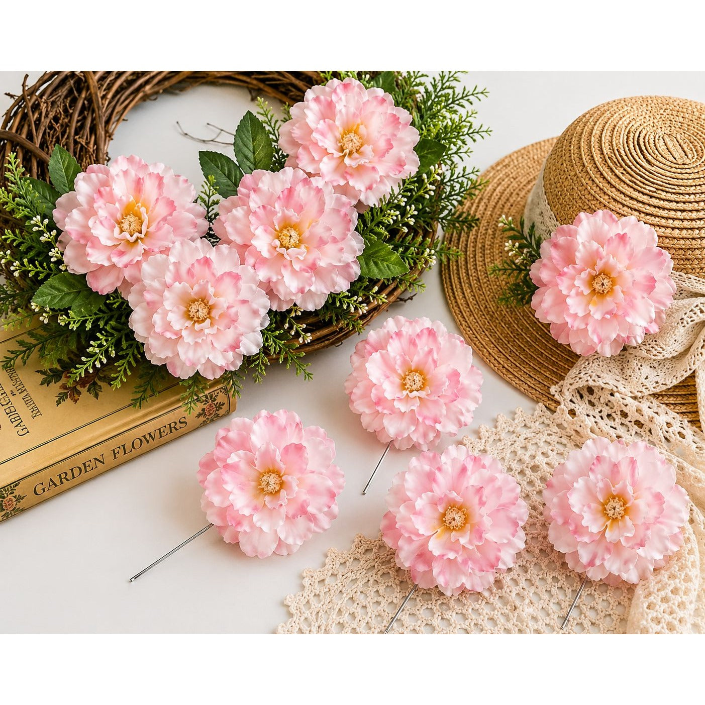 Pink artificial flowers on a white surface with a hat and books in the background