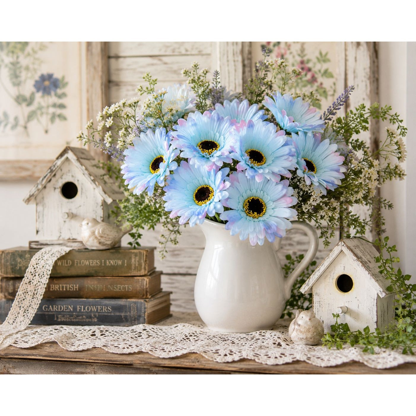 Bouquet of blue flowers in a white vase on a wooden table with birdhouses and books in the background.