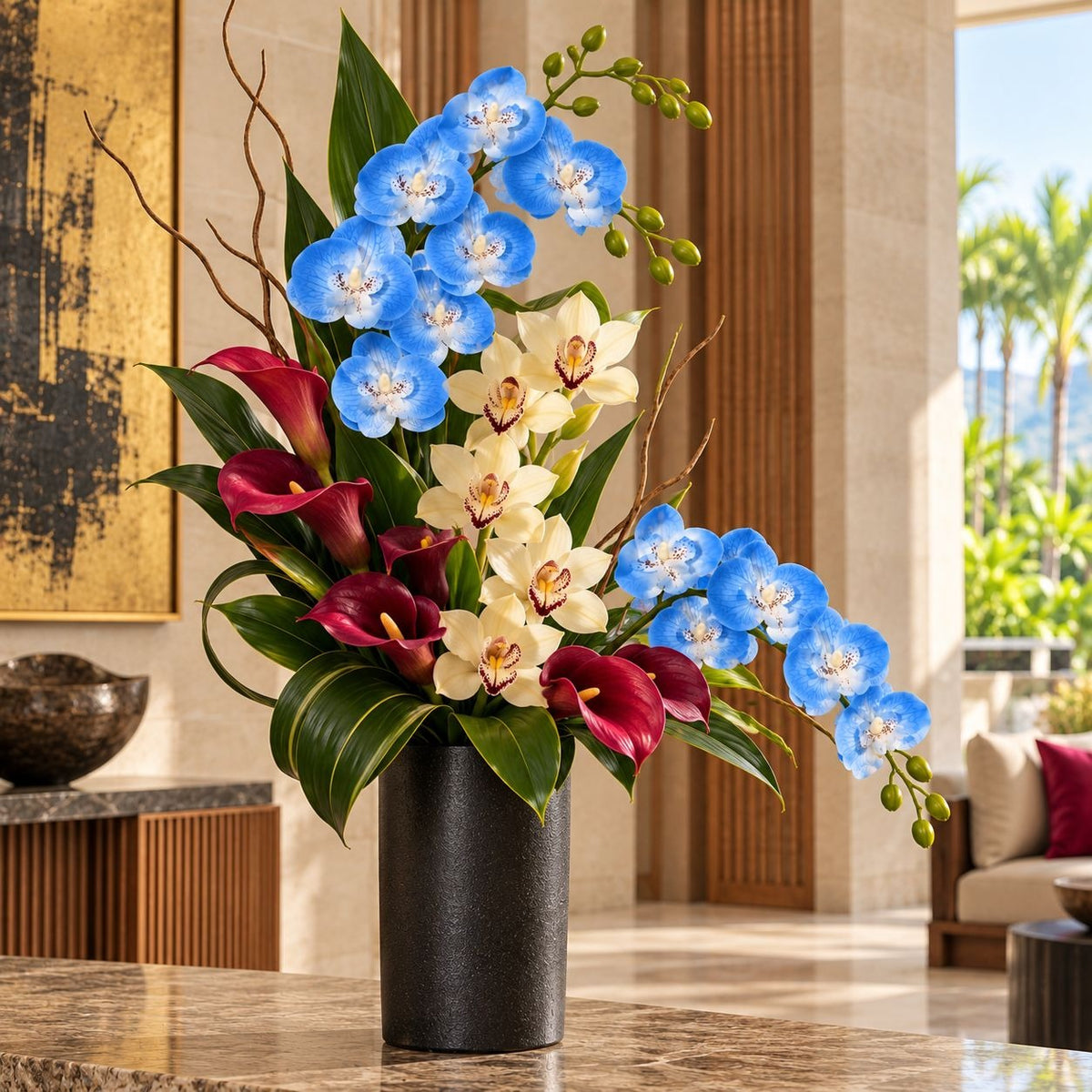 A vibrant artificial floral arrangement in a matte black cylindrical vase, featuring blue orchids, cream orchids, red calla lilies, and green leaves, set on a polished marble table in a luxurious modern interior.