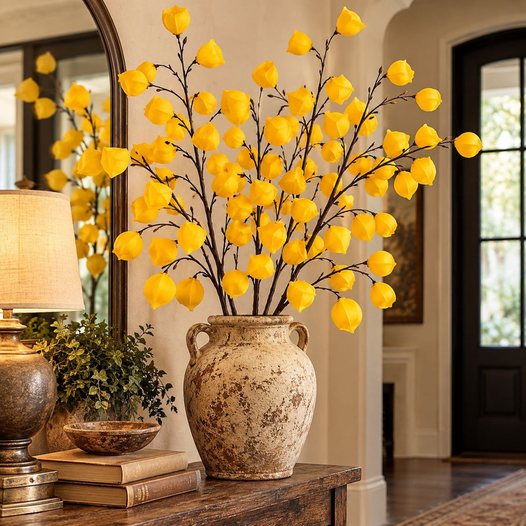 Yellow artificial flower branches arranged in a rustic beige ceramic vase on a wooden console table in a warm, elegant interior setting.