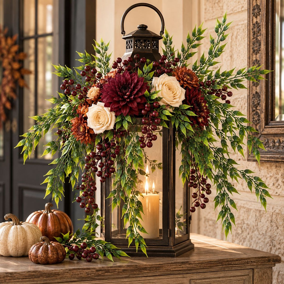 A decorative black metal lantern filled with a lit candle, surrounded by an autumn floral arrangement with burgundy dahlias, cream roses, green foliage, and dark berries, displayed on a wooden table in a rustic indoor setting.