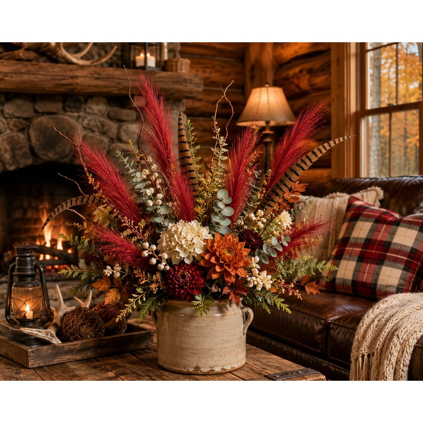 A rustic fall floral arrangement in a beige ceramic pot, displayed on a wooden table in a cozy log cabin living room with a fireplace, leather sofa, and plaid throw pillow.