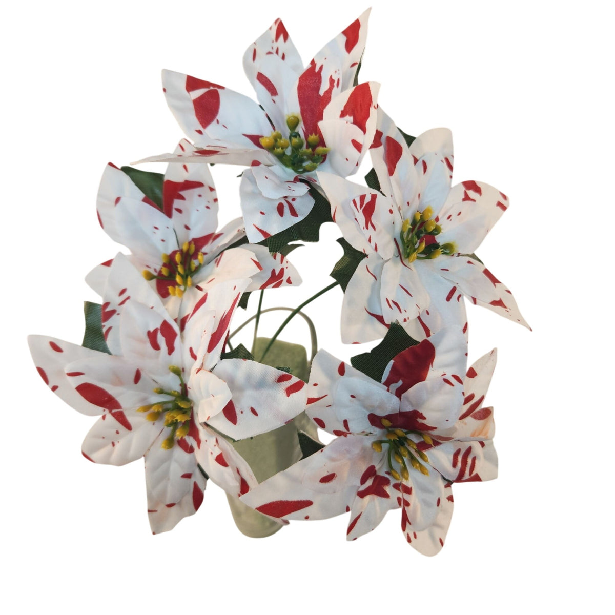 An artificial poinsettia wreath with white petals featuring red splatter patterns, green leaves, and yellow centers, arranged in a light green vase against a white background.
