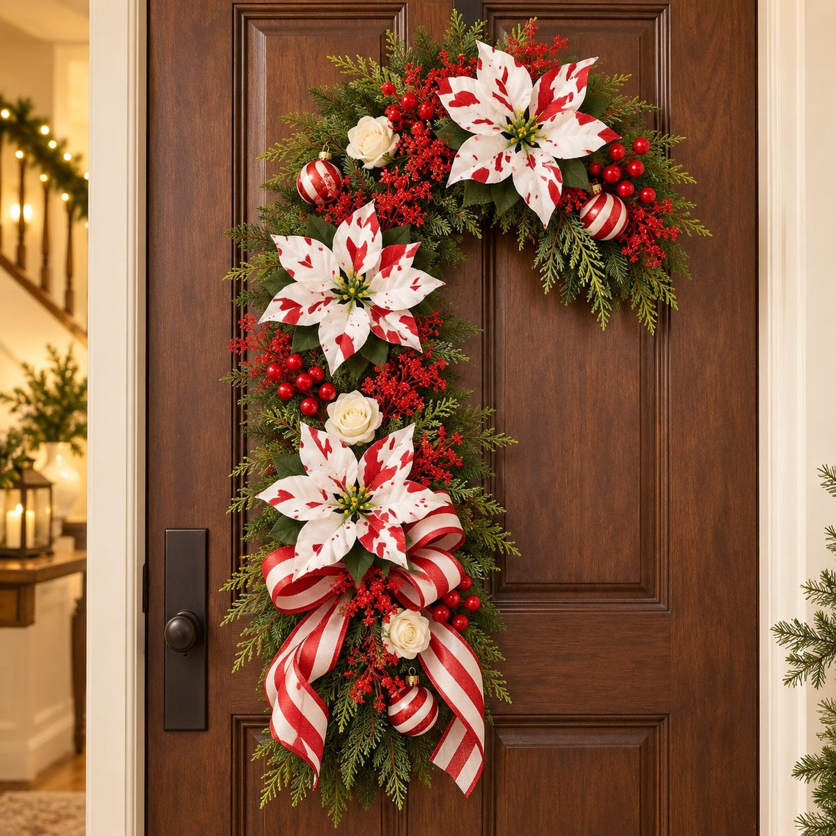 A festive holiday wreath hanging on a dark brown wooden door. The wreath features large white poinsettias with red stripes, red berries, green pine branches, and red-and-white striped ribbons.