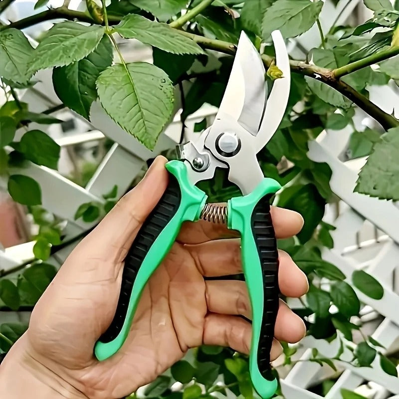 Hand holding green and black pruning shears with a garden background