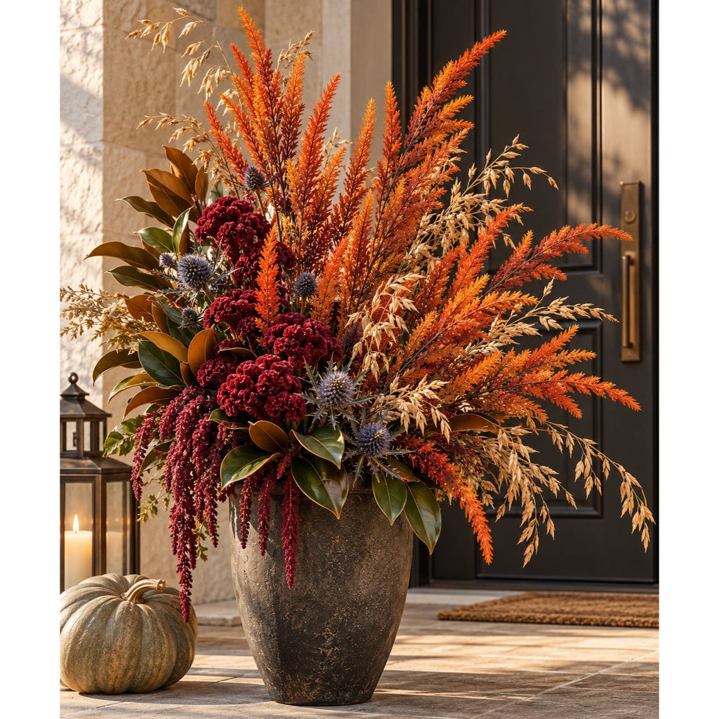 A large autumn floral arrangement in a tall textured gray pot, featuring orange and rust grasses, deep red berries, and green foliage, displayed on a front porch next to a small pumpkin.