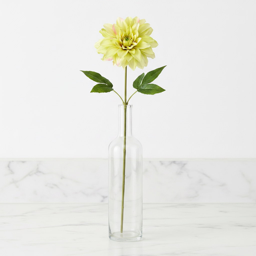 Single light green dahlia faux flower stem in tall clear glass vase on white marble countertop