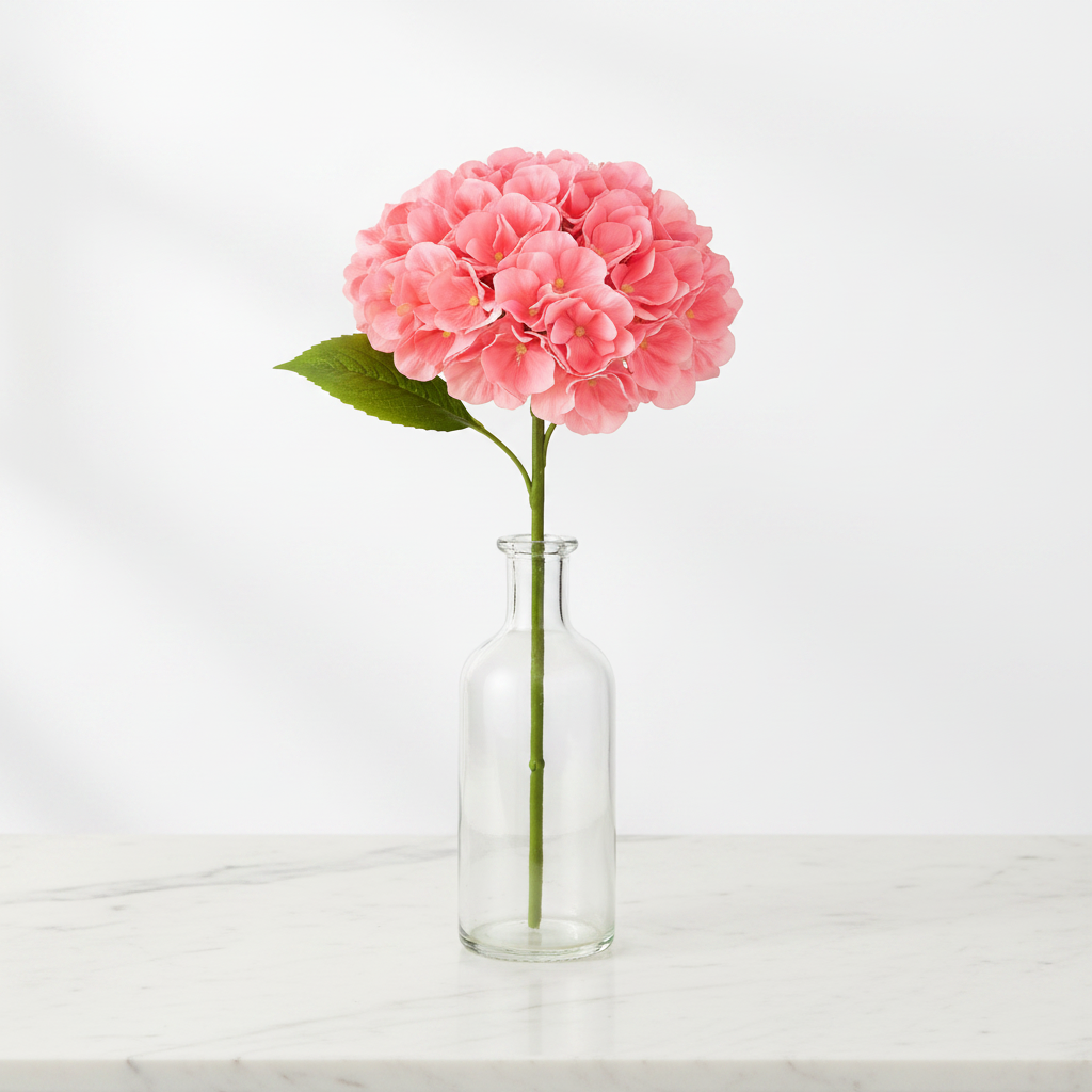 Coral pink artificial hydrangea stem in clear glass vase on white marble table elegant home decor styling no water