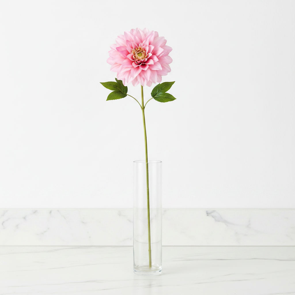Single soft pink dahlia faux flower stem in tall clear glass vase on white marble countertop