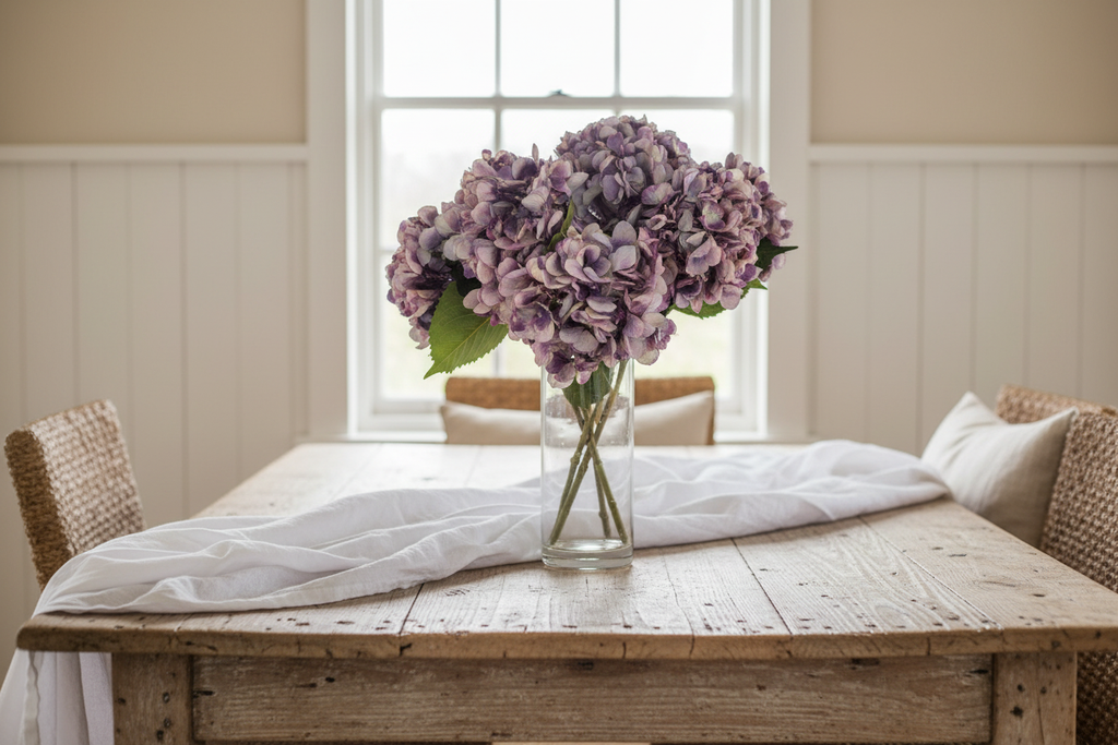 Farmhouse dining table with lavender purple hydrangea stems in glass vase with white linen and natural light