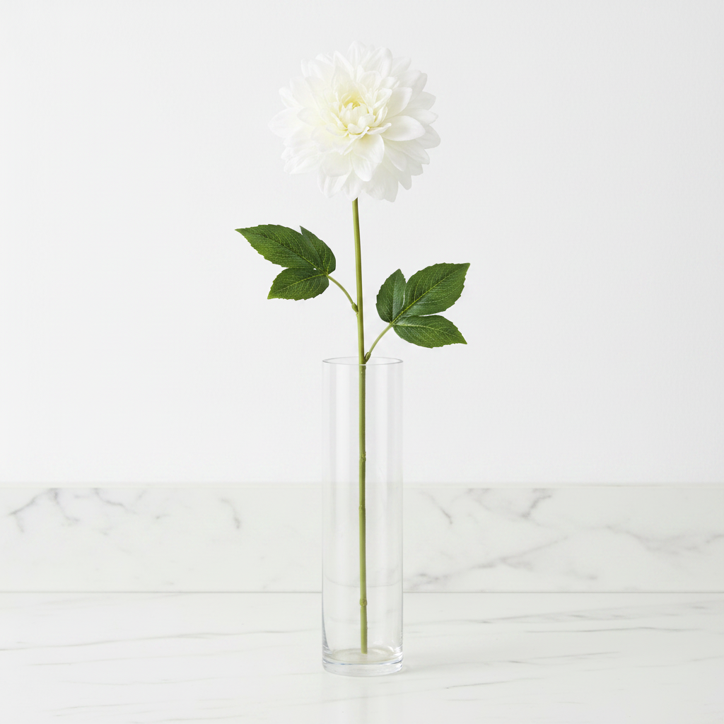 Single white dahlia faux flower stem with ivory center in tall clear glass vase on white marble countertop