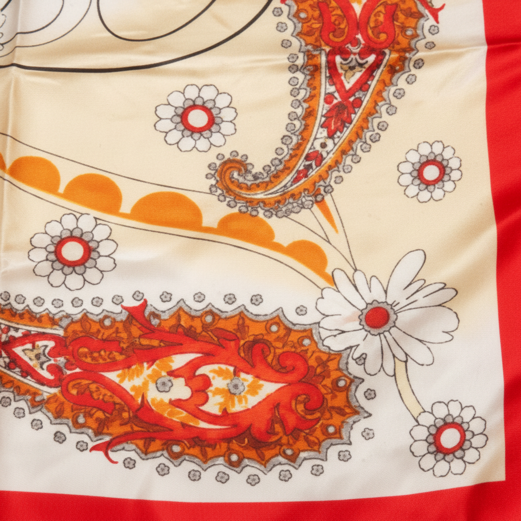 Close-up fabric detail of red paisley satin square scarf showing intricate red orange and gold paisley floral scroll pattern on cream background
