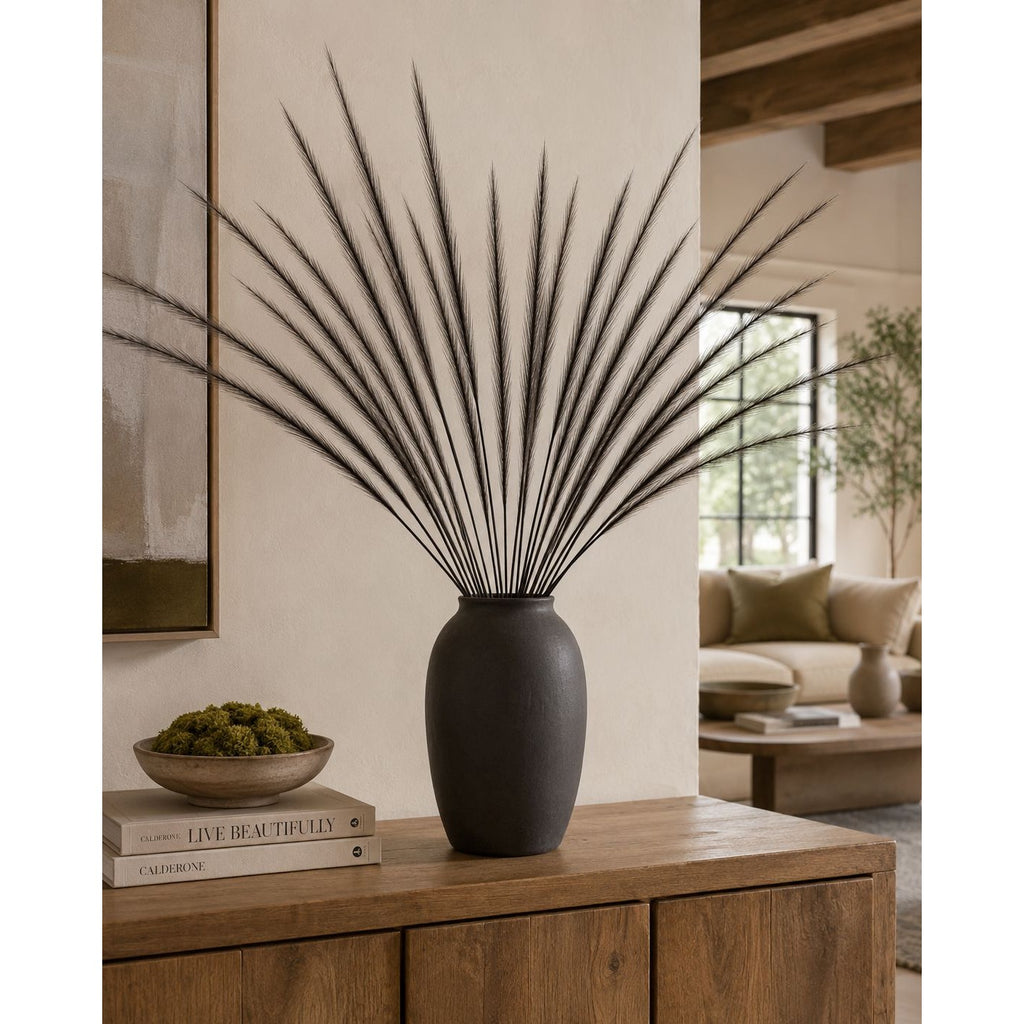 A dark charcoal gray ceramic vase holding a tall, spiky dried palm arrangement, styled on a wooden console table in a warm, modern living room setting.