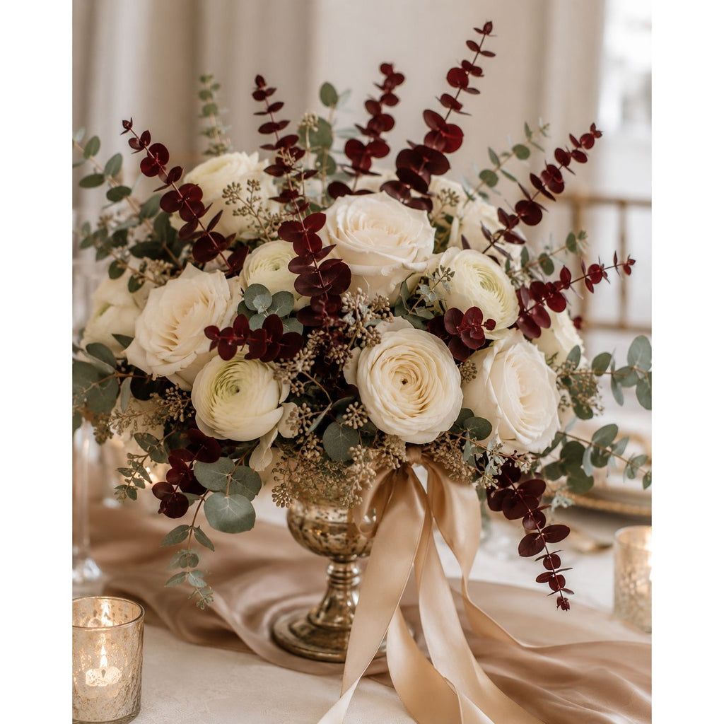Decorative floral arrangement with white roses, red berries, and greenery on a table with candles.